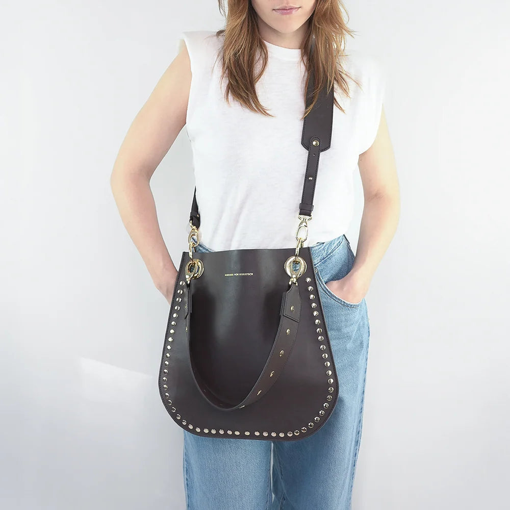 MALON Tasche in Schoko mit goldfarbenen Nieten und breitem Gurt, getragen als Crossbody-Tasche