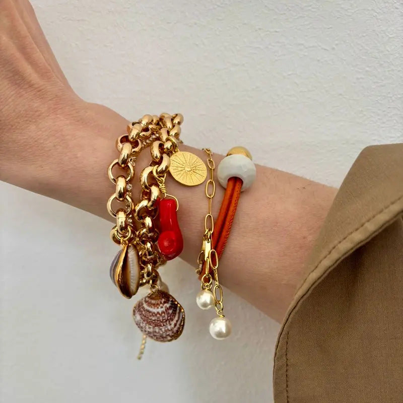 Goldenes Armband-Layering mit Charm-Armband, Muschelanhängern, Münzscheibe und orangefarbenem Lederarmband mit Perle